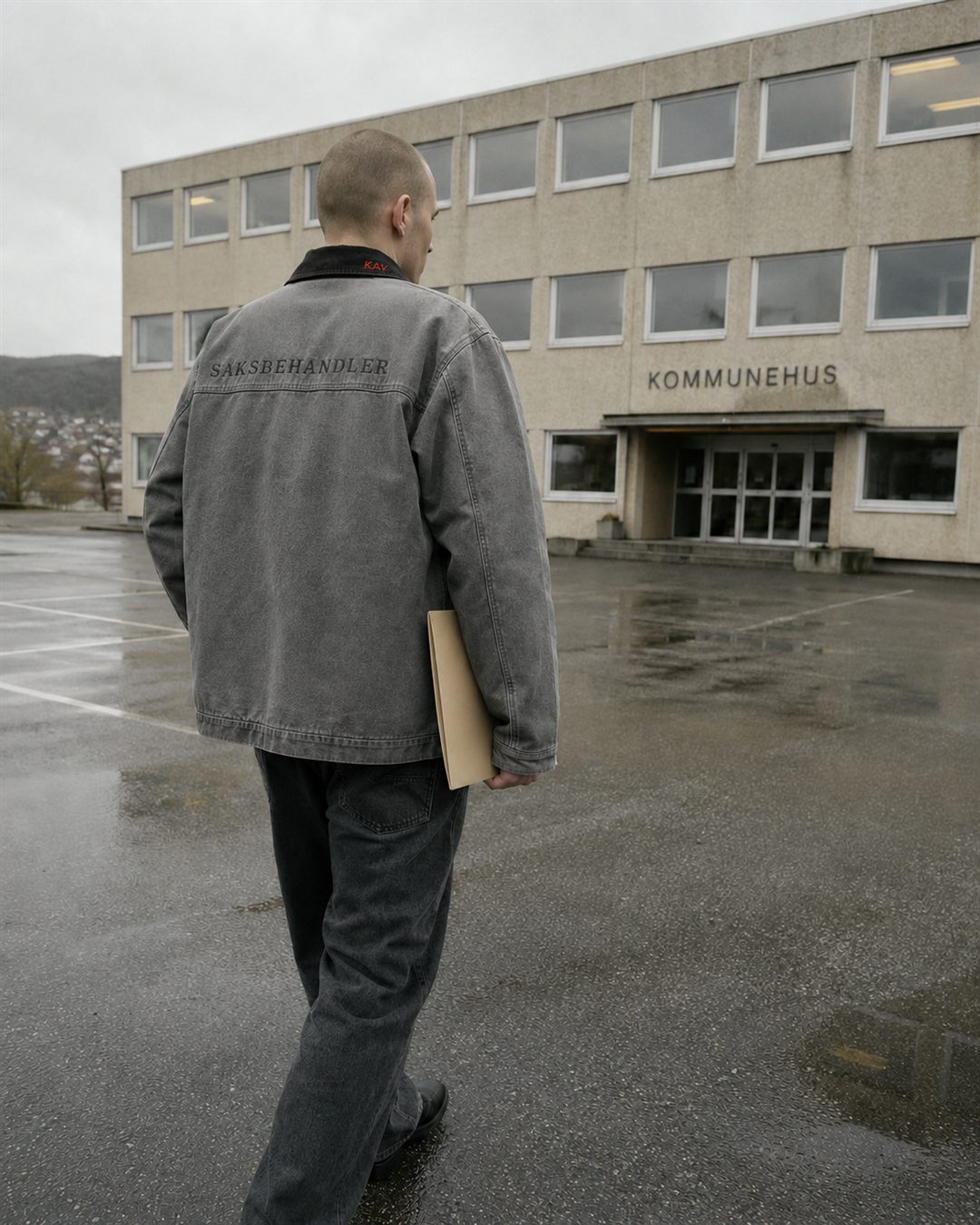 Modell bakfra i grå canvasjakke med teksten SAKSBEHANDLER over ryggen